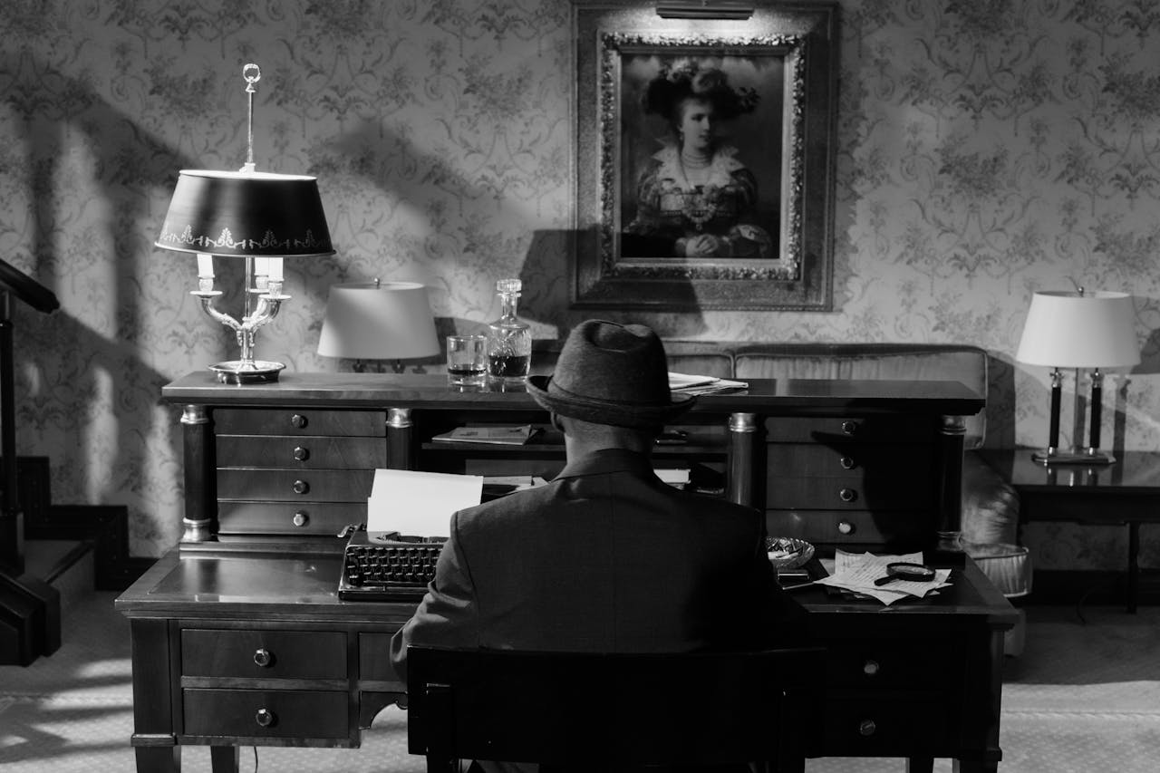 Home A vintage monochrome scene featuring a detective in a fedora hat at a typewriter, evoking classic noir mystery.